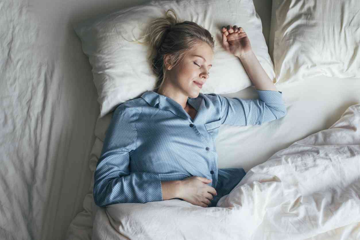 Lower Part of Female Body Wearing White Sleepwear Lying on Bed