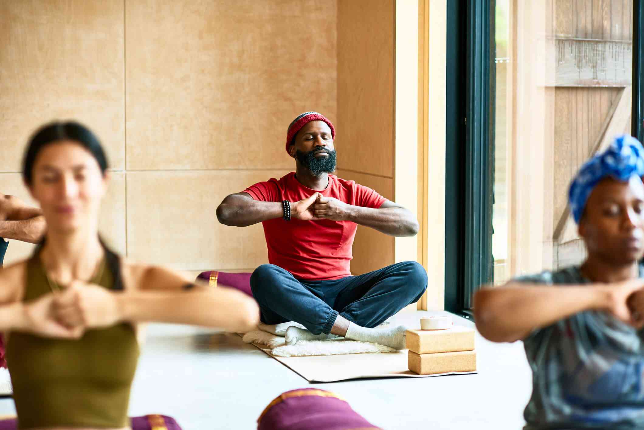 A man in a red shirt sits in a yoga class and practices some stretches to help reduce his anxiety.